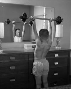 Boy exercising with dumbbell at mirror in bedroom